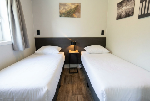 Tweepersoonskamer met twee eenpersoonsbedden, wit beddengoed en kunst aan de muur in Hackfort 4, Nederland.