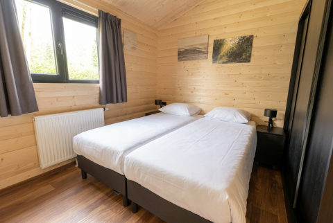 Schlafzimmer in einer Holzlodge mit zwei Einzelbetten, Fenster, Vorhängen und Wandbildern.