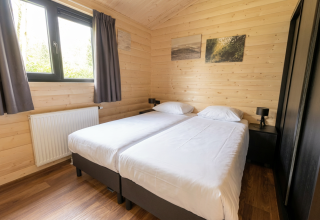 Slaapkamer in een houten lodge met twee aparte bedden, gordijnen, nachtkastjes en wandkunst.