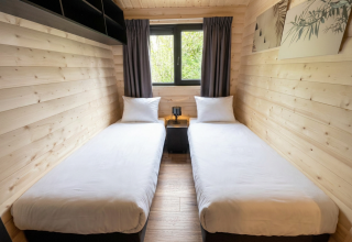 Modernes Lodge-Zimmer mit zwei Einzelbetten, Holzvertäfelung, Fenster mit Vorhängen und Wandkunst.