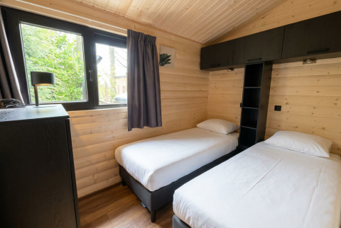 Gezellige slaapkamer in een houten lodge met twee enkele bedden, groot raam en zwarte kasten.