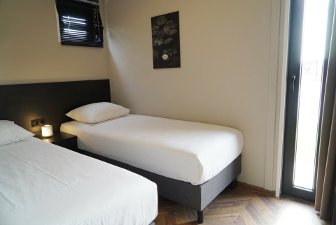 Twee eenpersoonsbedden in een eenvoudig ingerichte kamer bij Just Nature lodge, De Utrechtse Heuvelrug.