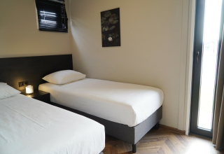 Twee eenpersoonsbedden in een eenvoudig ingerichte kamer bij Just Nature lodge, De Utrechtse Heuvelrug.