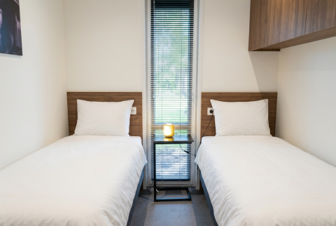 Moderne lodgekamer met twee enkele bedden, wit bedlinnen en een raam in L-Cube 4, De Utrechtse Heuvelrug.