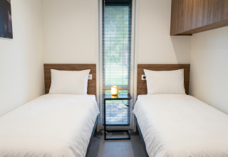 Moderne lodgekamer met twee enkele bedden, wit bedlinnen en een raam in L-Cube 4, De Utrechtse Heuvelrug.
