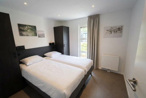 Moderne tweepersoonskamer met twee bedden, witte lakens en raam in L-Cube 4, De Utrechtse Heuvelrug, Nederland.
