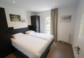 Moderne tweepersoonskamer met twee bedden, witte lakens en raam in L-Cube 4, De Utrechtse Heuvelrug, Nederland.