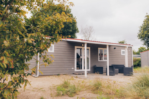 Exterior view of Dune Lodge, a cozy grey cabin with a porch and outdoor seating set in a green landscape.