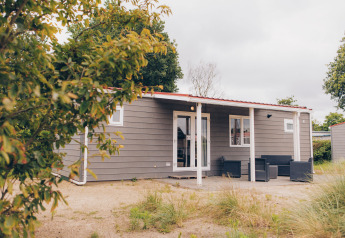 Außenansicht der Dune Lodge: Eine moderne, graue Hütte mit Veranda und Gartenmöbeln in natürlicher Umgebung.