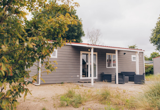 Exterior view of Dune Lodge, a cozy grey cabin with a porch and outdoor seating set in a green landscape.