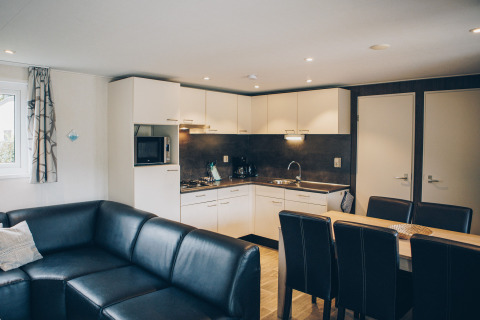 Modern open-plan lounge and kitchen in Dune Lodge, Duinhoeve, Netherlands, with black sofa and dining set.