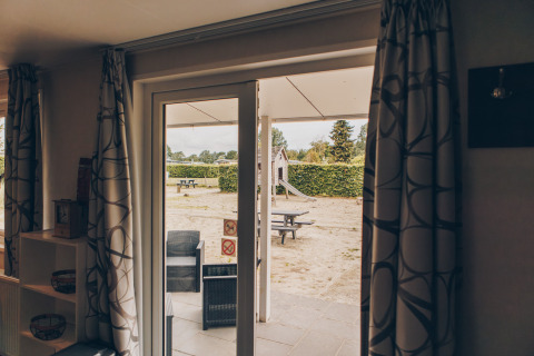 View from inside Dune Lodge at Duinhoeve, Netherlands, showing patio seating and a playground outside.