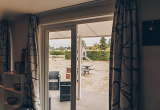 View from inside Dune Lodge at Duinhoeve, Netherlands, showing patio seating and a playground outside.