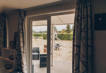 Vista dall'interno di Dune Lodge a Duinhoeve, Paesi Bassi, con area salotto e parco giochi fuori.