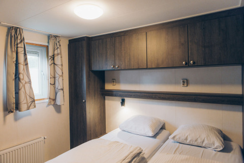 Cozy bedroom at Dune Lodge in Duinhoeve, Netherlands, featuring two beds, window, and wooden cabinets.
