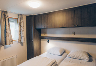 Cozy bedroom at Dune Lodge in Duinhoeve, Netherlands, featuring two beds, window, and wooden cabinets.