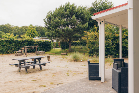 View of terrace and playground at Dune Lodge in Duinhoeve, Netherlands, surrounded by greenery and sand.
