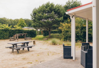 View of terrace and playground at Dune Lodge in Duinhoeve, Netherlands, surrounded by greenery and sand.