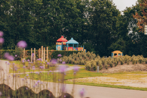Playground with colorful equipment at Dune Lodge, Duinhoeve, Netherlands, surrounded by greenery and trees.
