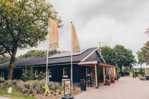 Front view of Dune Lodge at Duinhoeve, Netherlands, featuring a black building and two yellow flags.
