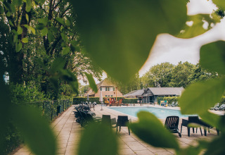View of the pool and Dune Lodge at Duinhoeve, Netherlands, seen through green leaves.