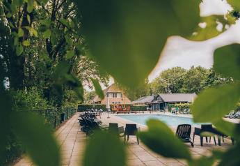 Blick durch grüne Blätter auf den Pool und die Dune Lodge bei Duinhoeve, Niederlande.