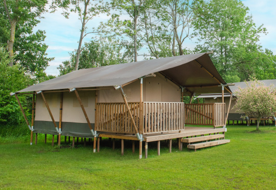 Safarizelt mit Holzveranda auf grüner Wiese, umgeben von Bäumen, perfekt für luxuriöses Camping.