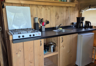 Kleine Küchenzeile in einem Safarizelt auf Camping De Rammelbeek in den Niederlanden mit Herd und Kühlschrank.