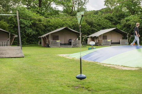 Safarizelte und Spielplatz auf dem Camping Dal van de Mosbeek in den Niederlanden mit grüner Umgebung.