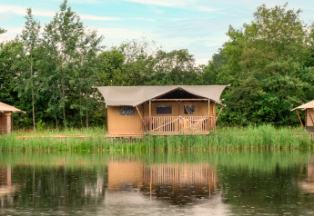 Safaritent aan het meer met sanitaire voorzieningen, omgeven door bomen en weerspiegeld in het water.