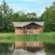 Tenda safari sul lago con servizi igienici, circondata da alberi e riflessa nell’acqua tranquilla.