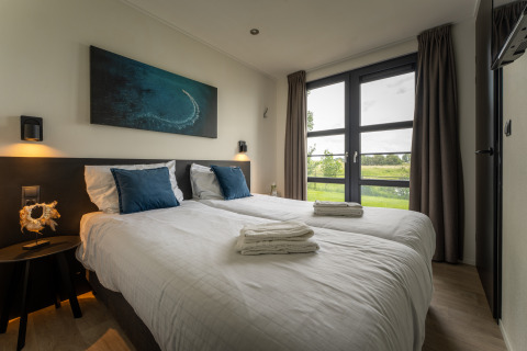 Modernes Schlafzimmer in der Villa Maritiem mit zwei Einzelbetten, großen Fenstern und Gartenblick.