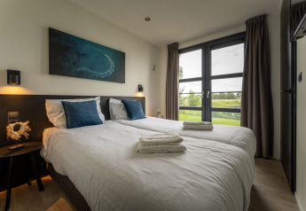 Moderne slaapkamer bij Villa Maritiem met twee enkele bedden, grote ramen en zicht op het groen.