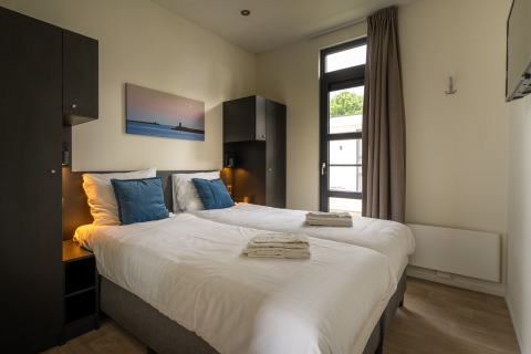 Modernes Doppelzimmer in der Villa Maritiem Lodge mit weißen Betten, blauen Kissen und Fensterblick.