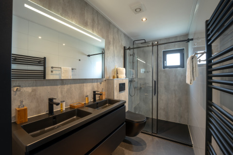 Modernes Badezimmer in der Villa Maritiem mit Doppelwaschbecken, Glasdusche und schwarzen Akzenten.