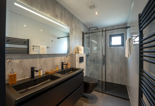 Modernes Badezimmer in der Villa Maritiem mit Doppelwaschbecken, Glasdusche und schwarzen Akzenten.