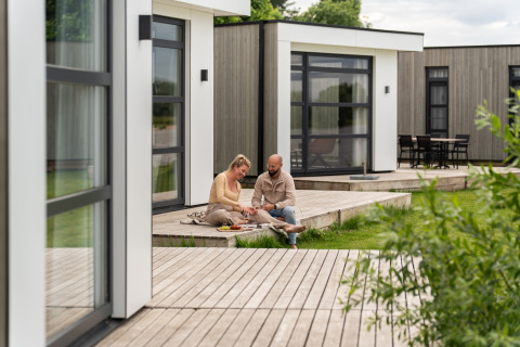 Paar auf Holzterrasse vor Villa Maritiem im MarinaPark Bad Nederrijn, moderne Lodges, Niederlande.