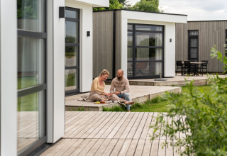 Paar auf Holzterrasse vor Villa Maritiem im MarinaPark Bad Nederrijn, moderne Lodges, Niederlande.