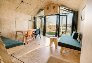 Tiny house moderne avec intérieur en bois minimaliste, grandes fenêtres et vue sur un espace vert.