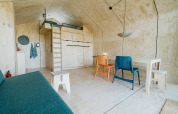 Interior luminoso de casa pequeña con altillo, sillas coloridas y decoración de madera en Wikkelhouse Bear, Países Bajos.