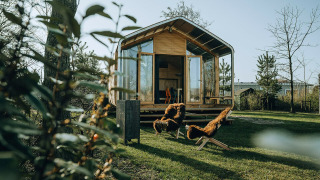 Moderna tiny house Wikkelhouse Bear con grandes ventanales y dos sillas cubiertas de piel en el césped.