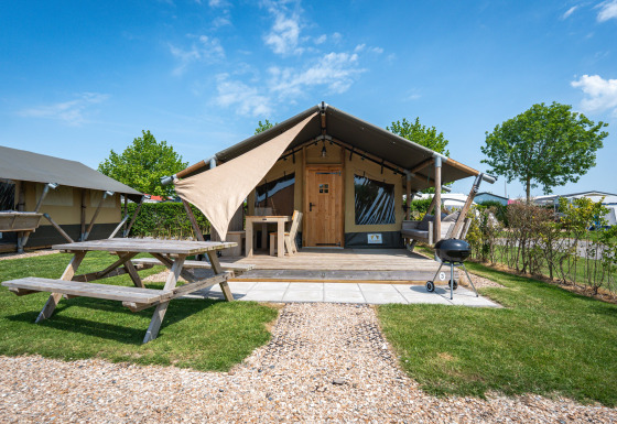 Afbeelding van een safaritent Compact met houten terras, picknicktafel en barbecue op een zonnige camping.