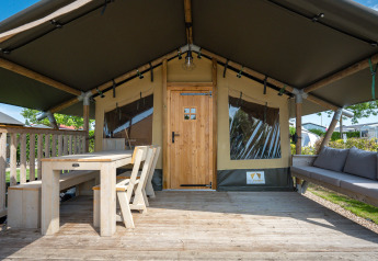 Safari tent ‘Compact’ at Camping de Molenhoek, Netherlands, featuring a wooden porch, table and comfy bench.