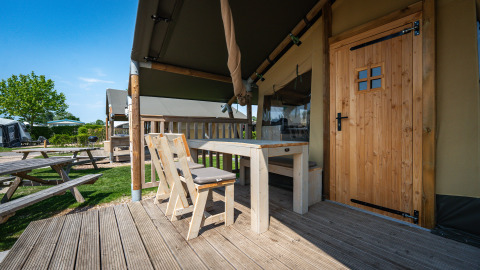 Veranda con tavolo e sedie in legno davanti a una tenda safari al Camping de Molenhoek, Paesi Bassi.