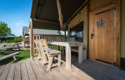 Houten terras met tafel en stoelen bij een safaritent op Camping de Molenhoek in Nederland, onder blauwe lucht.