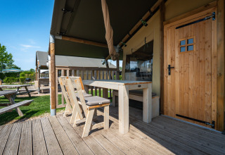 Houten terras met tafel en stoelen bij een safaritent op Camping de Molenhoek in Nederland, onder blauwe lucht.