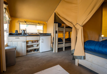 Compact safari tent at Camping de Molenhoek, Netherlands, featuring a small kitchen, bunks, and table.