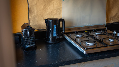 Zwart keukenblad met koffiemachine, waterkoker en gasfornuis in een safaritent op Camping de Molenhoek.