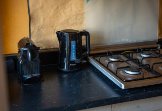 Piano cucina nero con macchina da caffè, bollitore elettrico e fornello a gas in tenda safari al Camping de Molenhoek.
