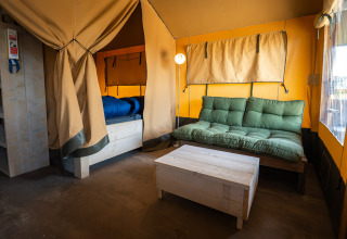 Interno della tenda safari Compact al Camping de Molenhoek nei Paesi Bassi, con divano e letto.